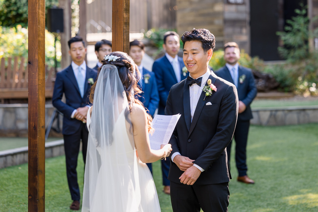 groom joyfully looking at his bride while she gives her vows
