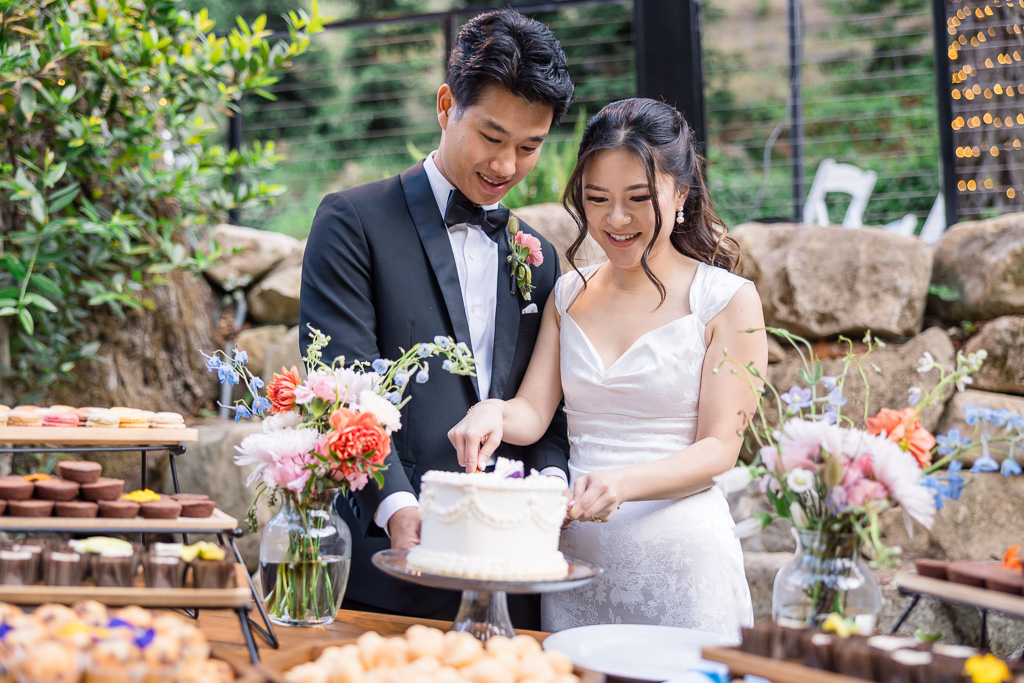 bride and groom cutting their wedding cake on a colorful dessert table