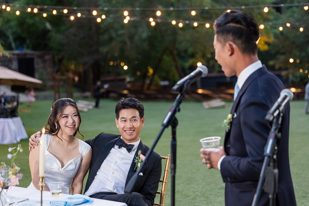 bride and groom looking on as groom's brother gives a toast