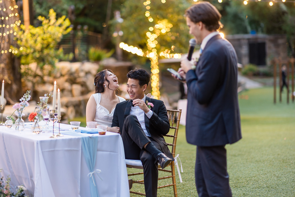 the newlywed couple cracking up at a joke told by the best man during dinner toast