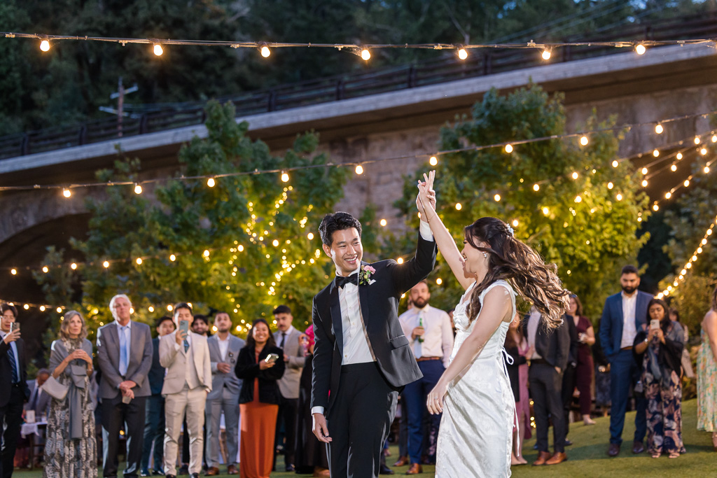 spinning the bride around under string lights with all the wedding guests watching from afar