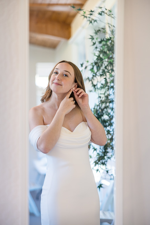 bride putting on earrings in front of a mirror