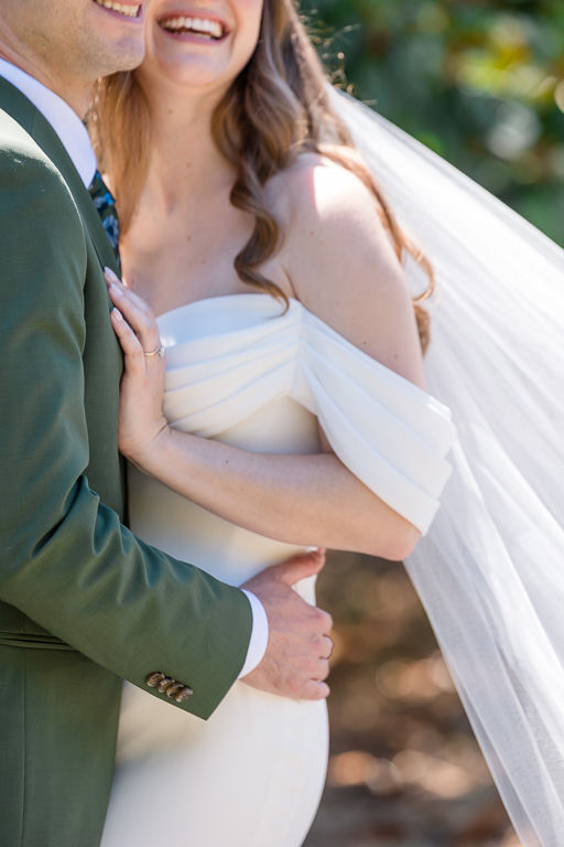 close-up partial body photo of the bride and groom showing off suit, dress, and veil