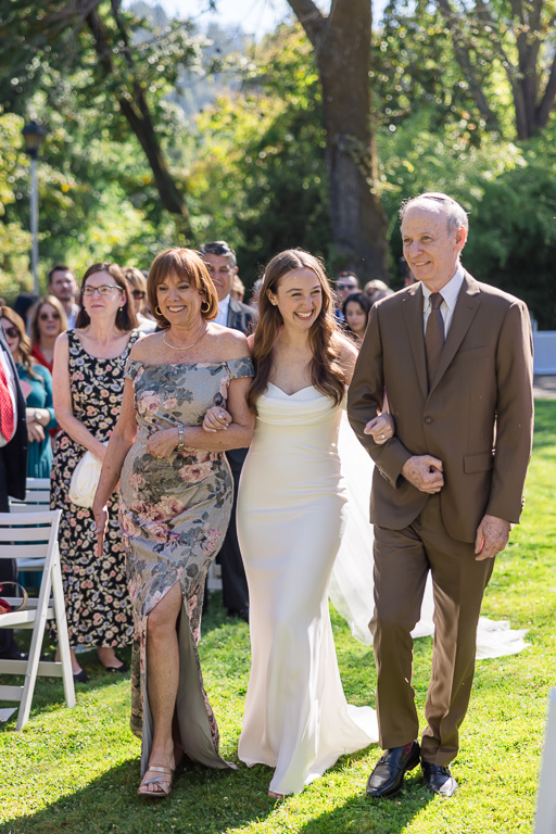 a happy bride flanked on both sides by her mom and dad walking down the wedding aisle