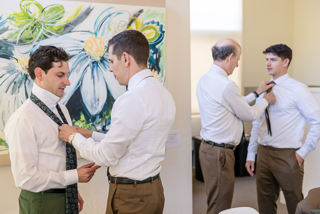 groom getting his tie adjusted by a groomsman while dad helps a different groomsman