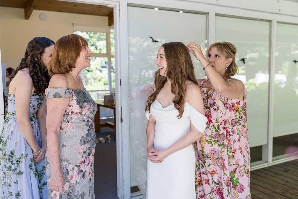 bride laughing and talking with bridesmaids while mom puts veil into her hair
