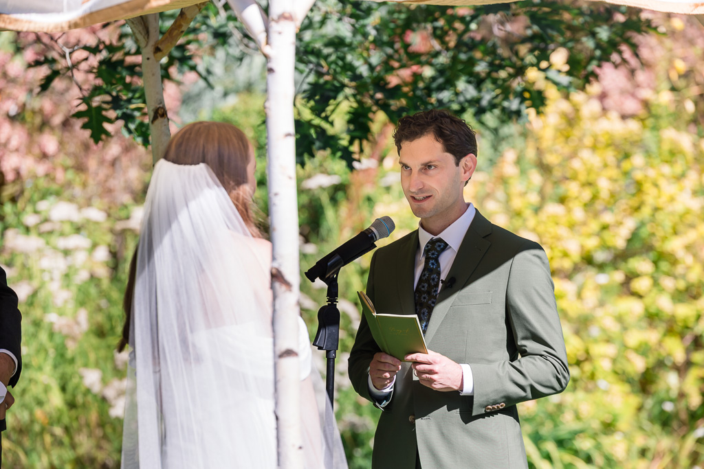 groom reading his written vows under a chuppah