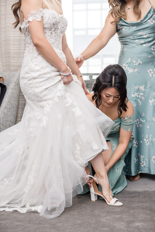 sister and bridesmaids helping bride with her wedding shoes