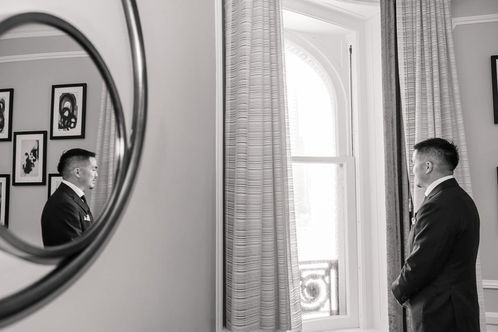 cool photo of groom looking out a window and a mirror reflection of him in the same frame