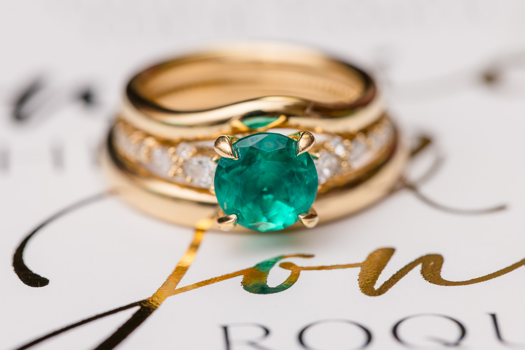 close-up photo of emerald engagement ring and wedding bands