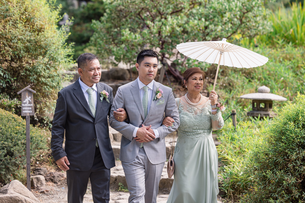 groom entering the ceremony flanked by both of his parents