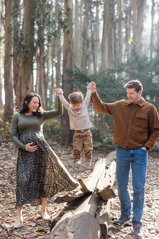 mom and dad swinging two year old over a log
