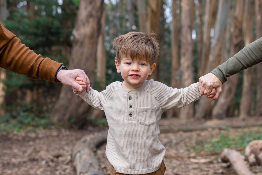 two year old kid in the woods holding hands with his parents