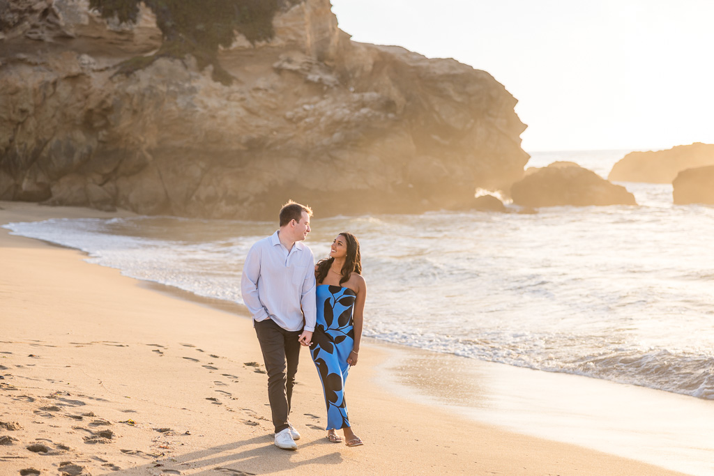 walking along the beach at golden hour with a blue and black dress