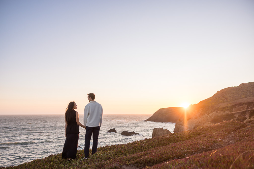 engagement photo of couple looking out over the ocean as the sun hits the horizon