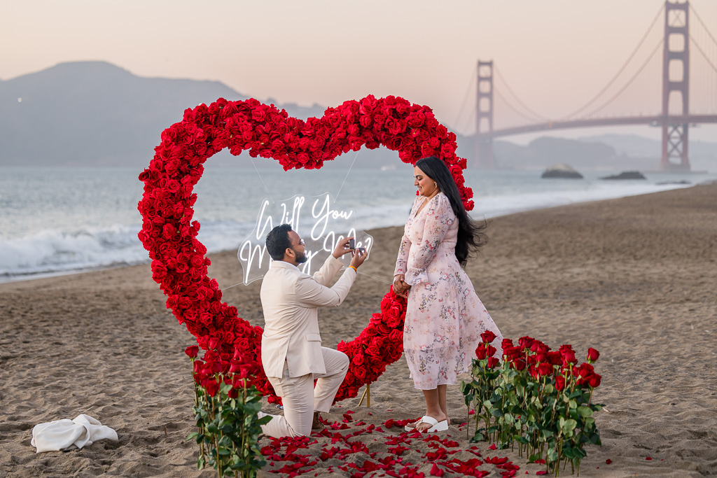 Marriage proposal on Baker Beach with a floral rose heart arch behind them