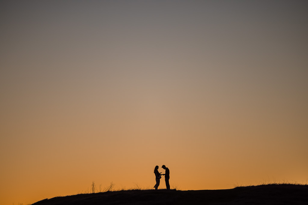 silhouette of newly-engaged couple taking a phone photo of her new ring