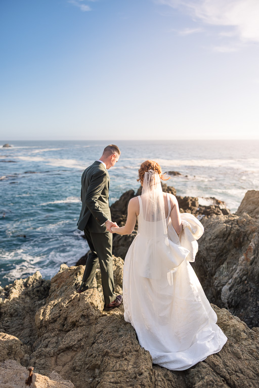 couple walking along the rocks over the ocean at sunset