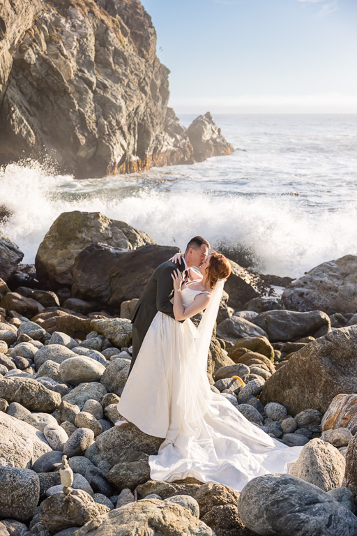 wedding photo of couple on rocks with waves crashing behind them