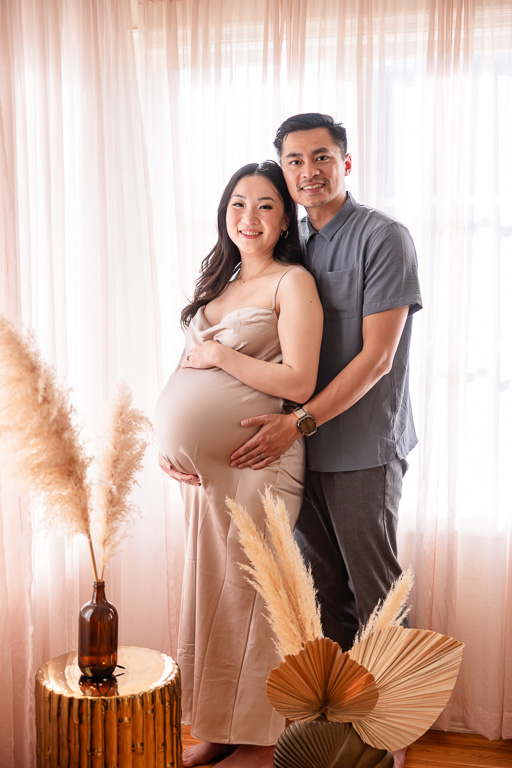 husband and wife maternity photo with soft indoor lighting and curtains