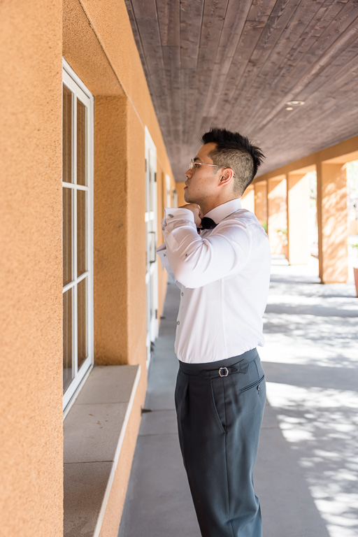 the groom adjusting his bow tie against a window