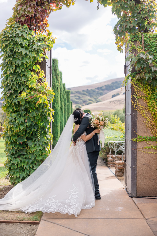bride and groom hugging near tall lush arch