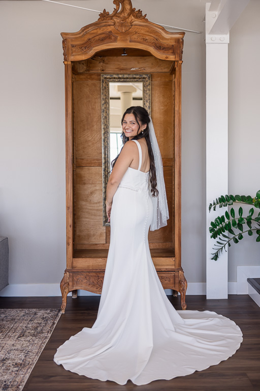 bride standing in front of a wooden dresser with a mirror