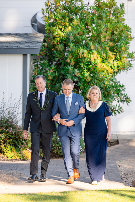 groom walking towards the wedding ceremony with both of his parents