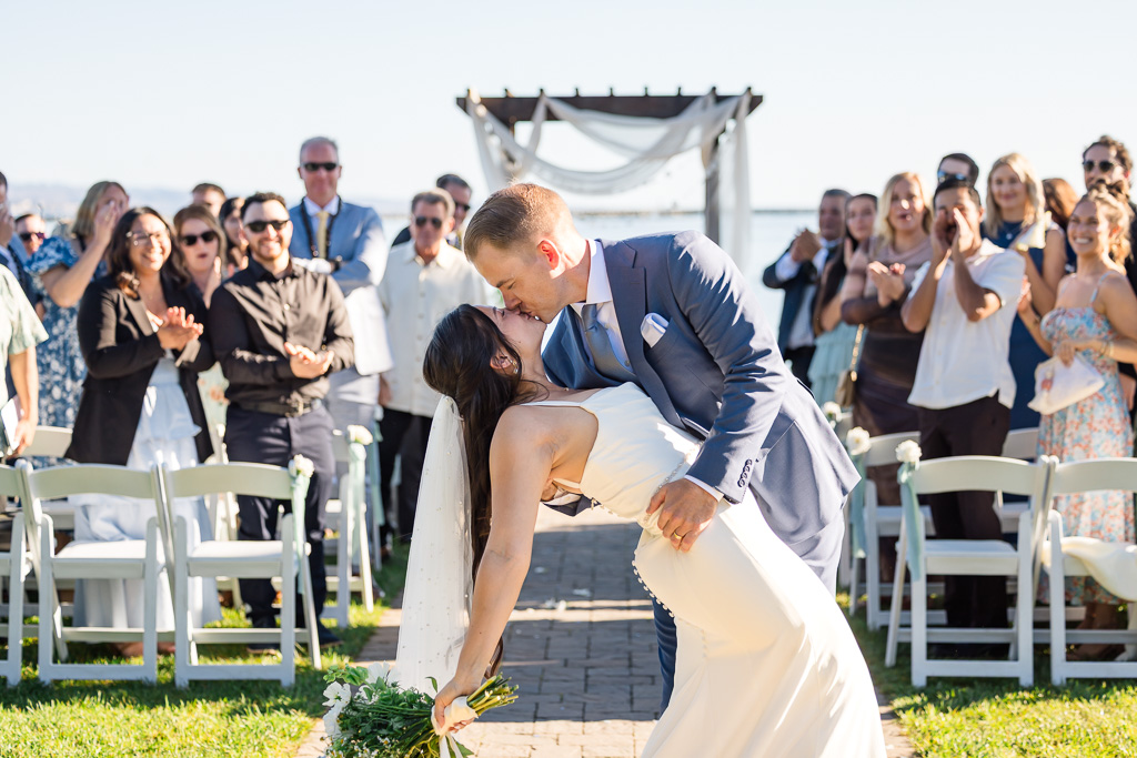 bride and groom dip and kiss at the end of the aisle after their recessional, with guests looking on in the background