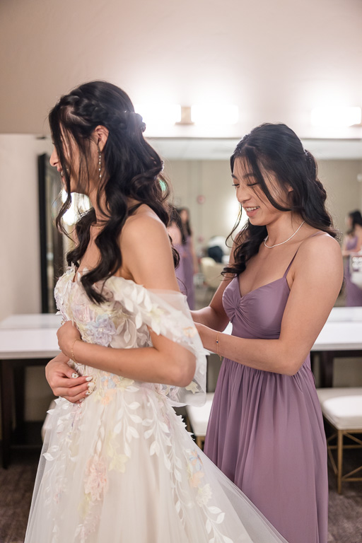 sister of the bride buttoning up the back of the bride's dress