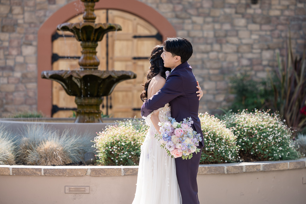 Bride and groom embracing by fountain