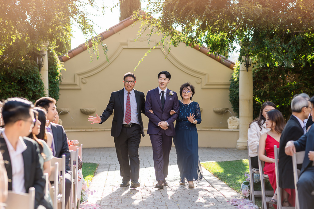 Groom walking down aisle with parents during ceremony