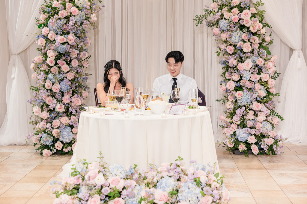 Bride and groom seated at sweetheart table with floral arrangements