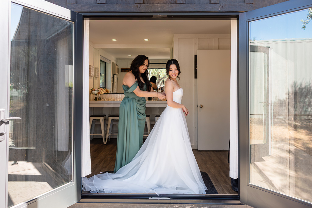 a bridesmaid helping the bride button up her dress at MOHI Ranch