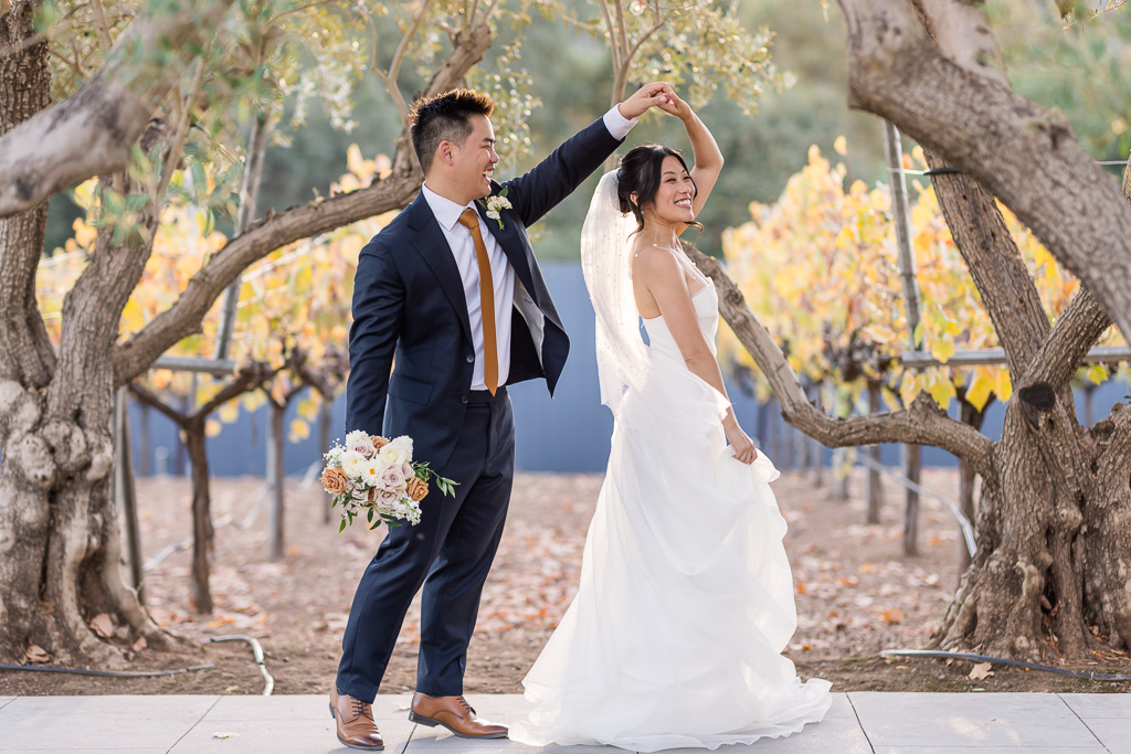 couple doing a little dance on their wedding day under some trees