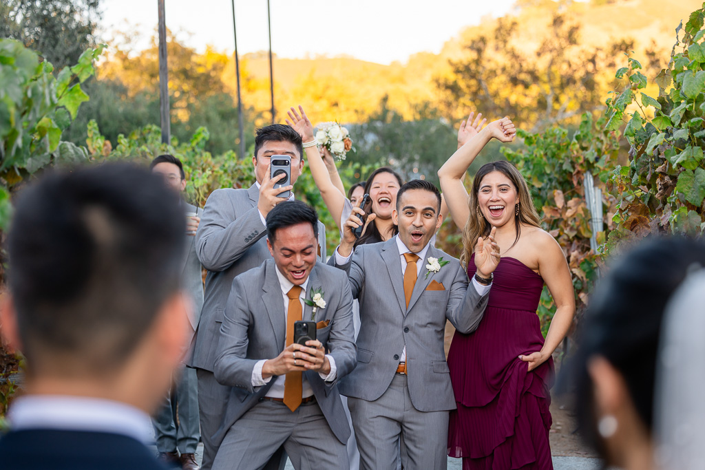wedding party excitedly taking photos and greeting the bride and groom