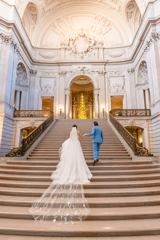 wedding photo walking up San Francisco City Hall grand staircase with long veil train trailing behind