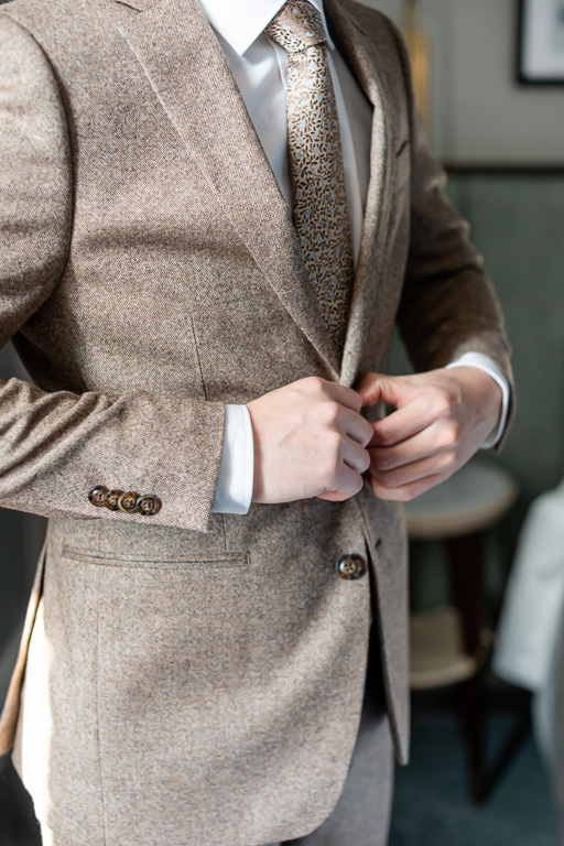 close-up of groom buttoning up his suit