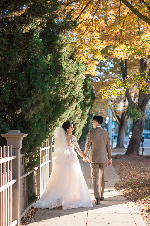 candid wedding photo of the couple walking away from the camera under orange and yellow leaves