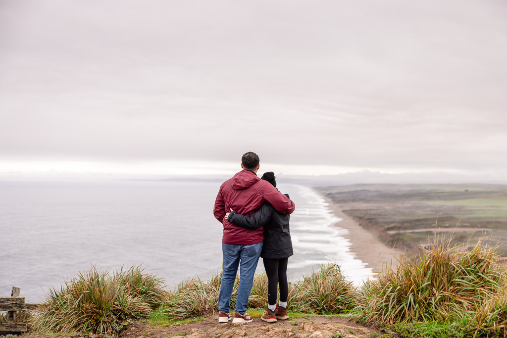 couple standing atop an ocean cliff overlook, enjoying the view below