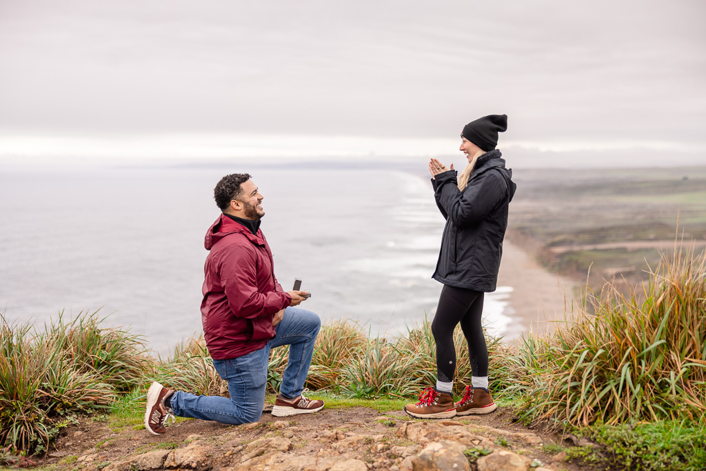 cute engagement proposal on a cliffside above a long ocean beach