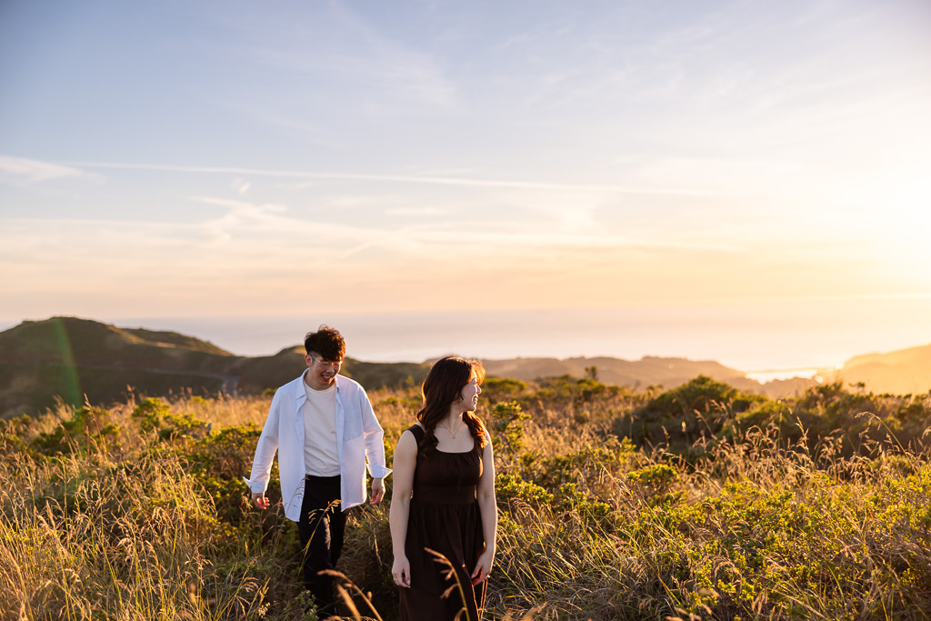 candid unposed photo of couple walking through golden field of grass under a sunset sky