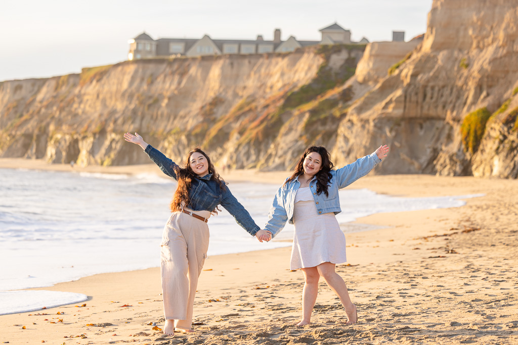 sisters holding hands on the beach for a photo