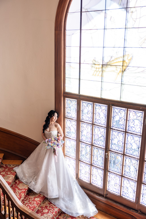 wide, dramatic, classic portrait of bride leaning against large backlit stained glass window