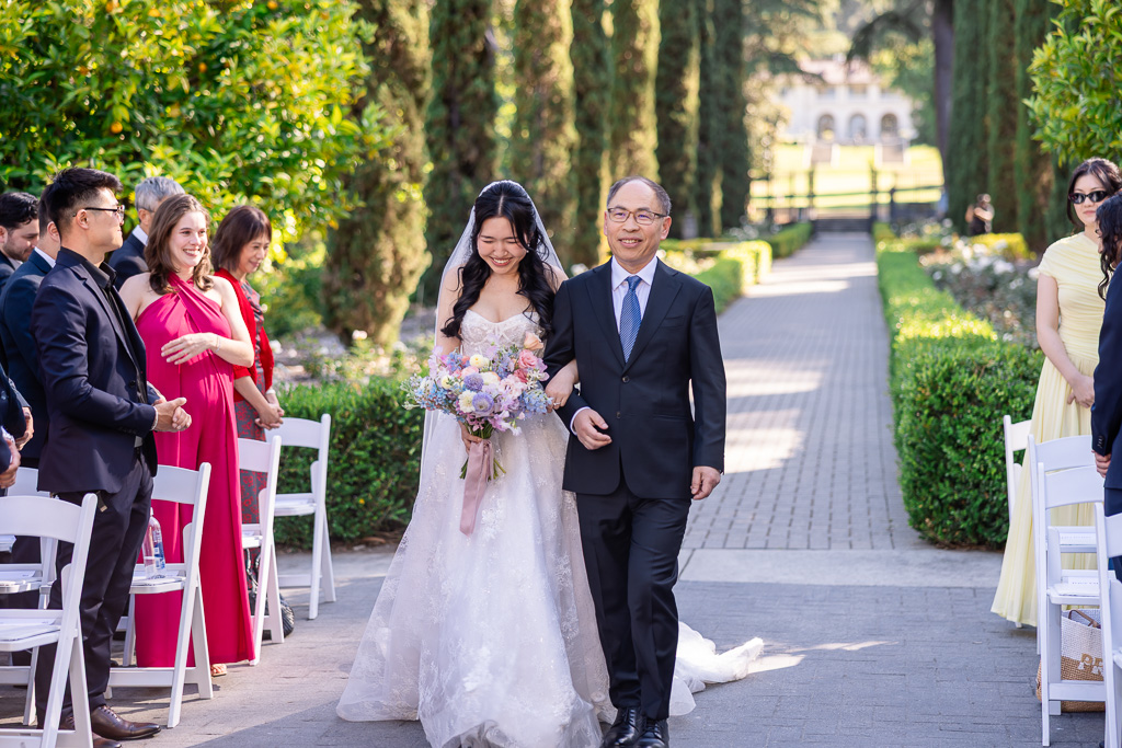 guests looking on as the bride walks down the aisle escorted by her dad
