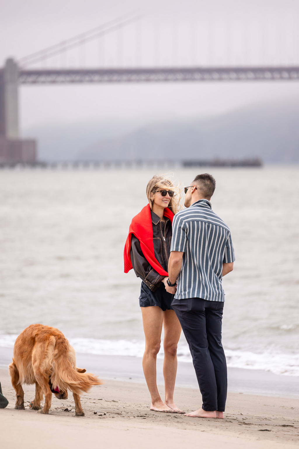 couple standing on the beach near the Golden Gate Bridge on a windy, foggy day