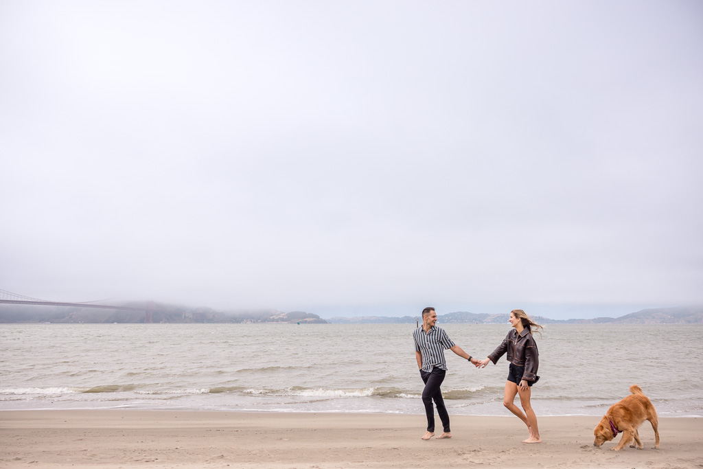 couple walking along the beach with their dog behind them