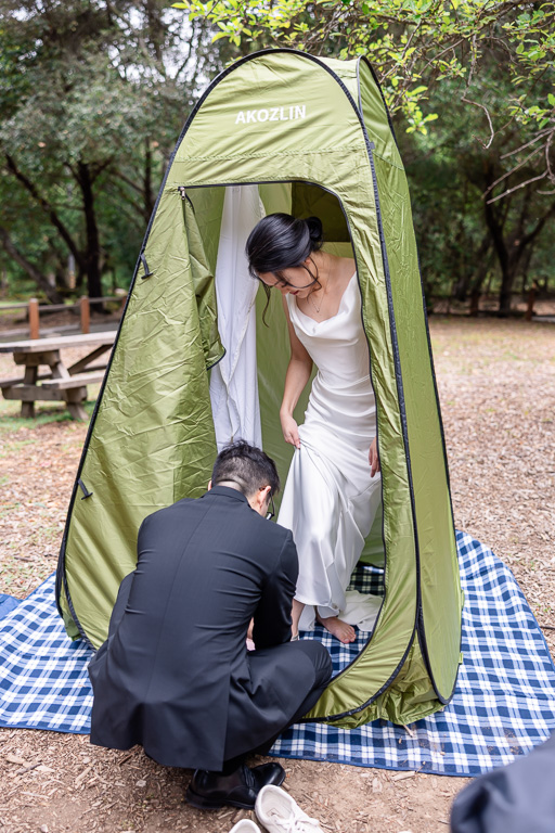 groom helping bride put on her shoes in a pop-up tent for a casual wedding