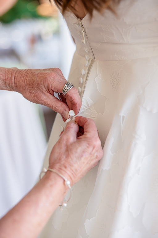 bride's mom helping her button up wedding dress
