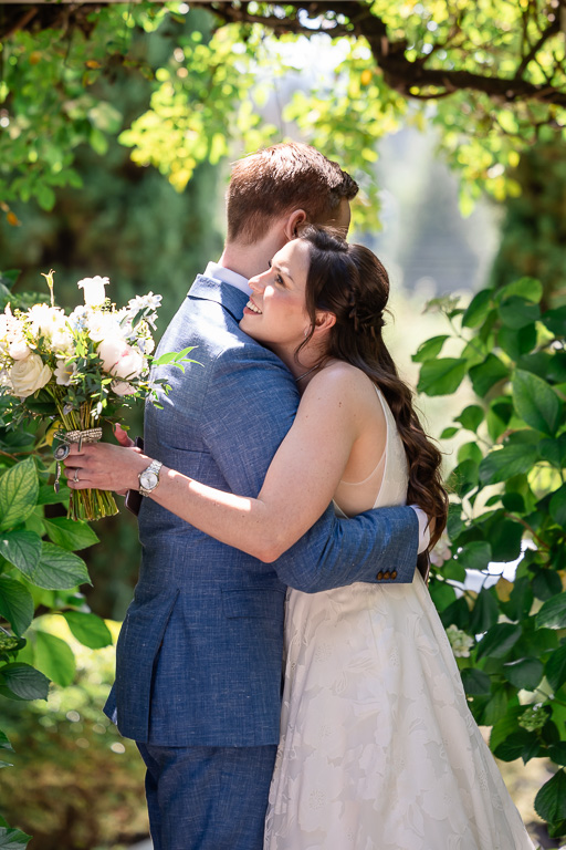 bride and groom hugging in a lush green garden under some trees